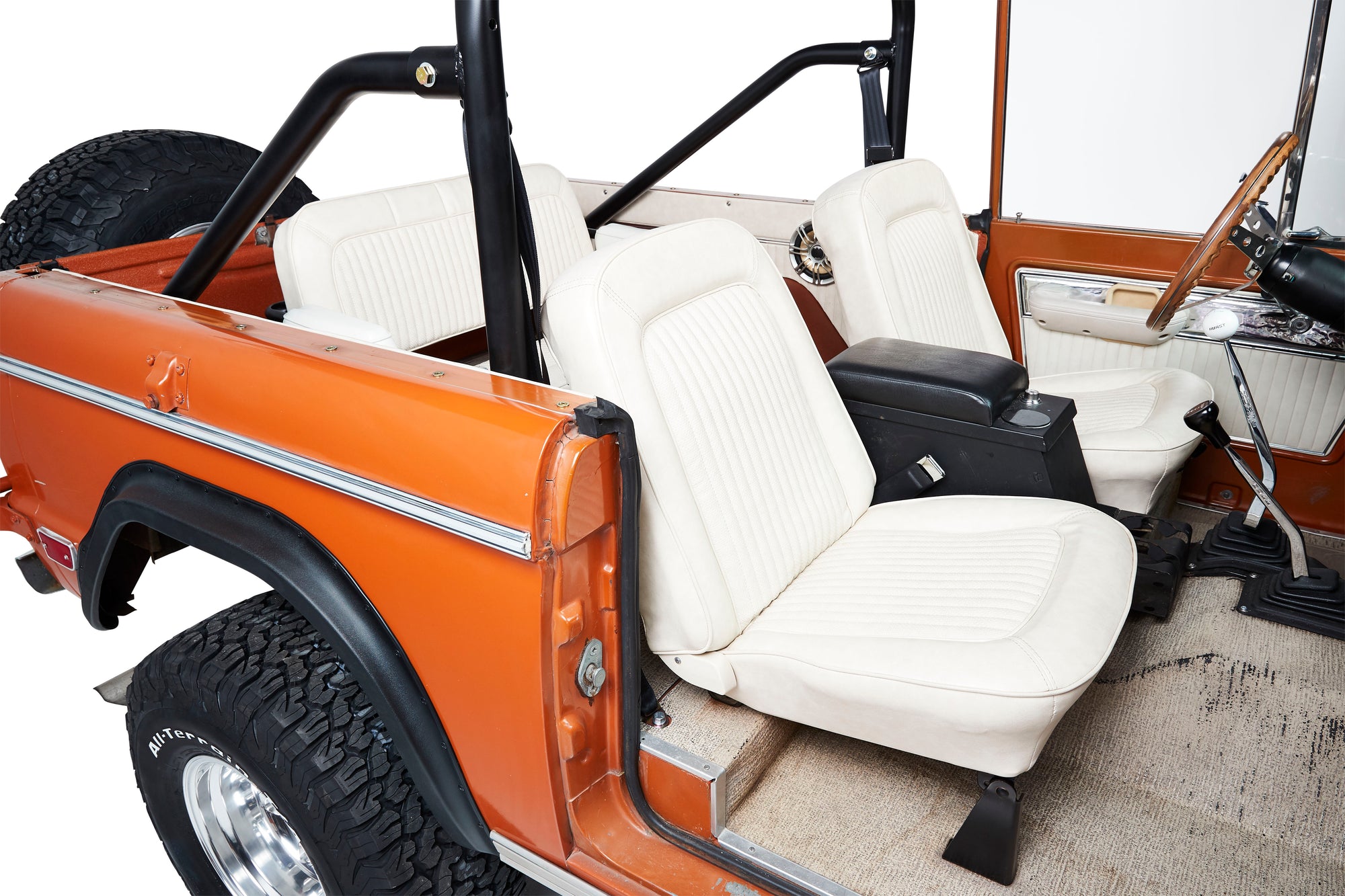 Classic Ford Bronco interior with white seats, orange body, roll bar, and off-road tires.