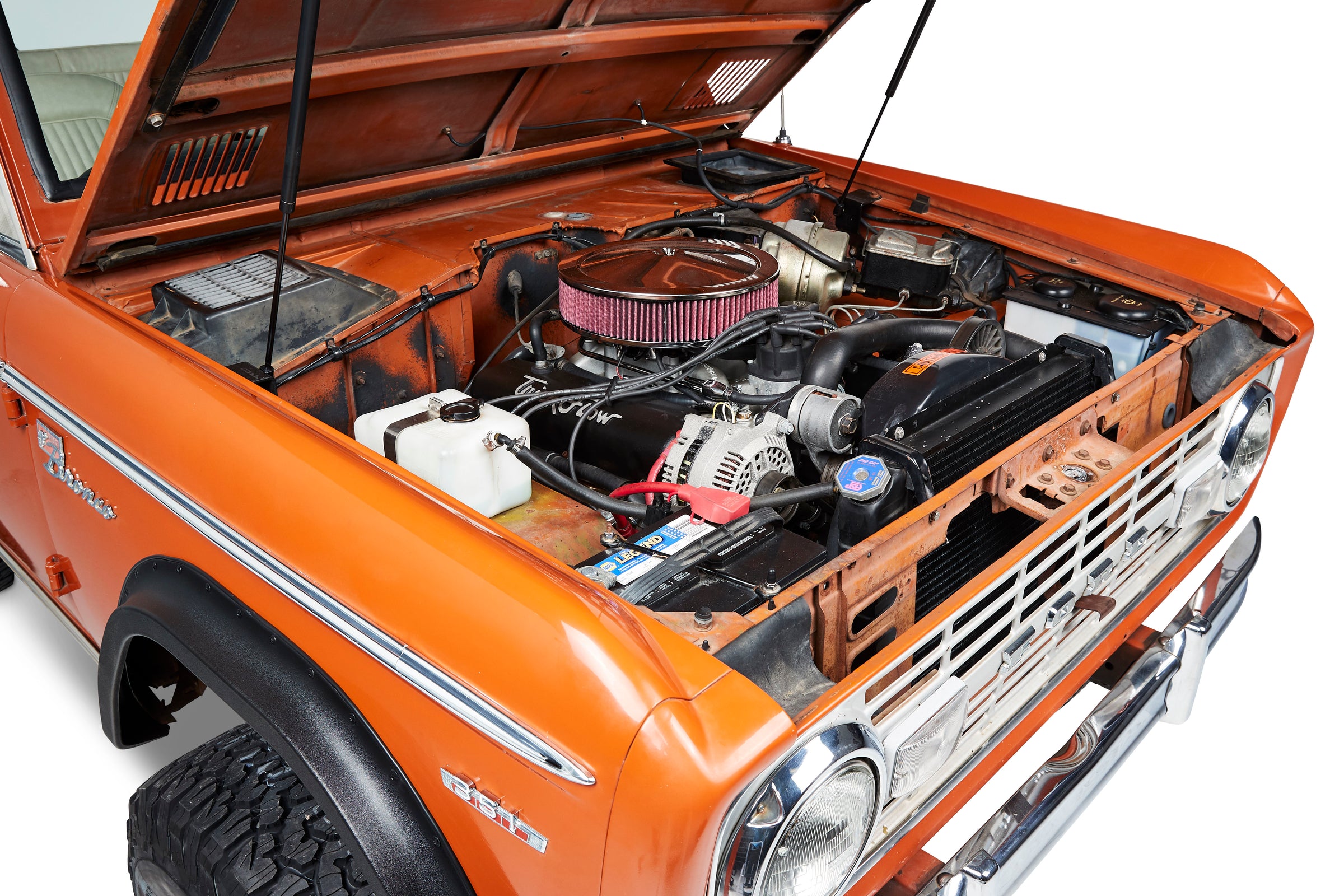 Open hood showing engine compartment and orange exterior of Classic Ford Bronco