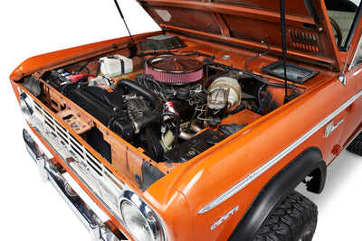 Classic Ford Bronco with open hood showing detailed view of engine compartment and orange exterior.