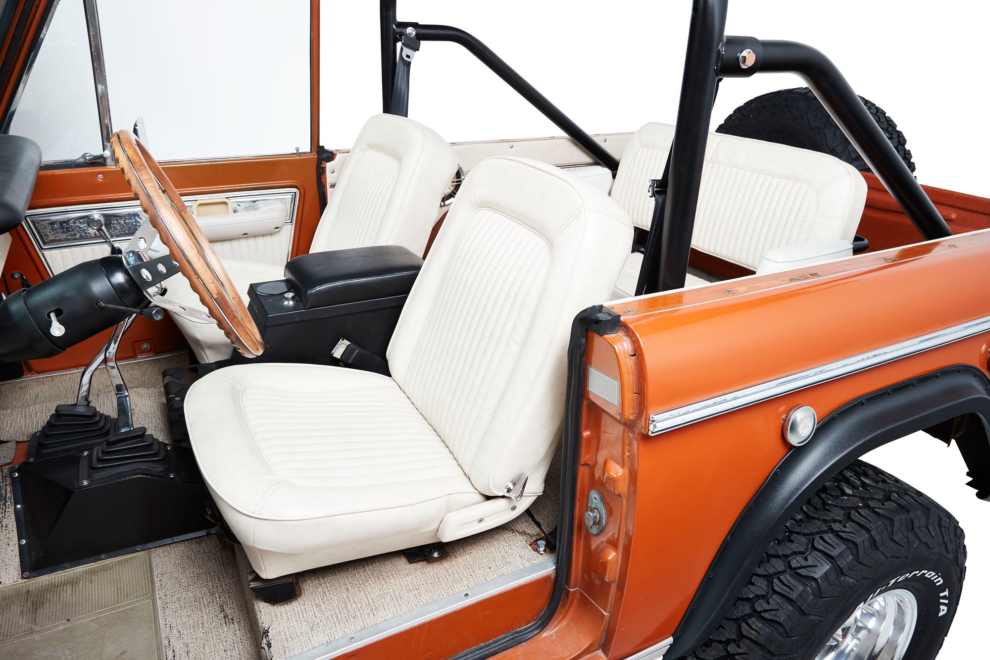 Interior view of a Classic Ford Bronco showing white seats, wooden steering wheel, and orange door panel.