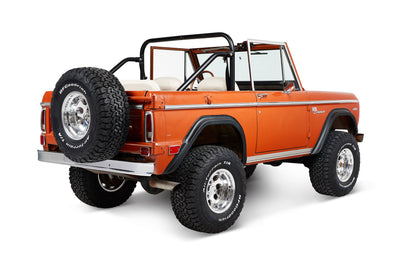 Three-quarter rear view of orange Classic Ford Bronco with open top and white seats.