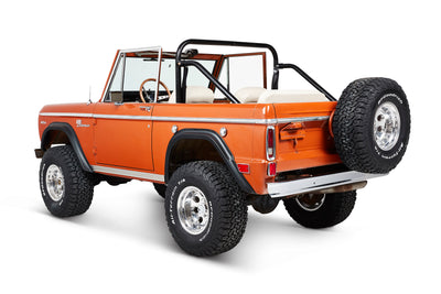Three-quarter rear view of orange Classic Ford Bronco highlighting spare tire on tailgate.