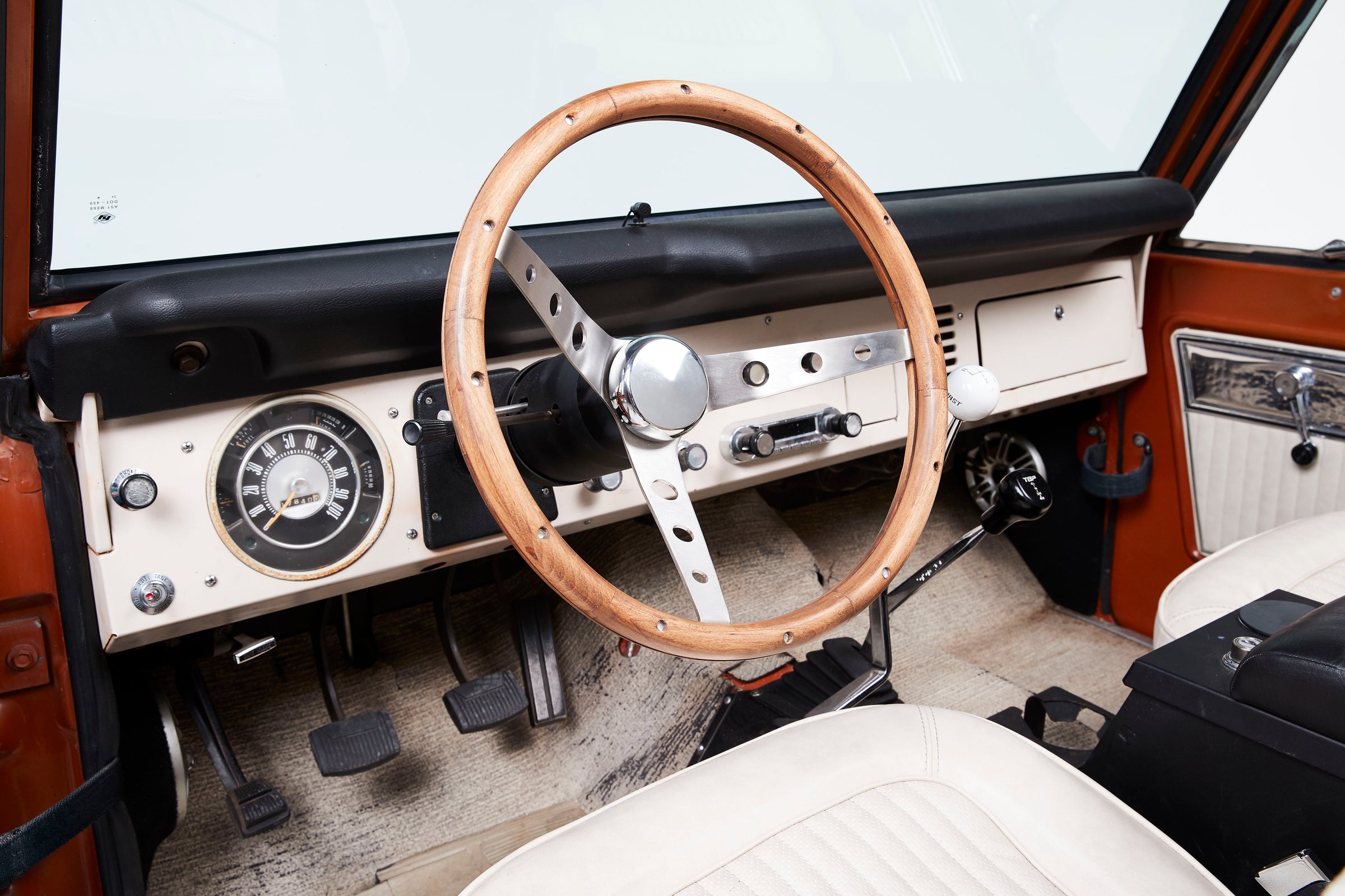 Interior view showing wooden steering wheel, white seats, and dashboard controls in Classic Ford Bronco.