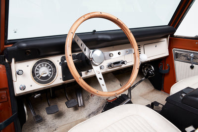 Interior view showing wooden steering wheel, white seats, and dashboard controls in Classic Ford Bronco.
