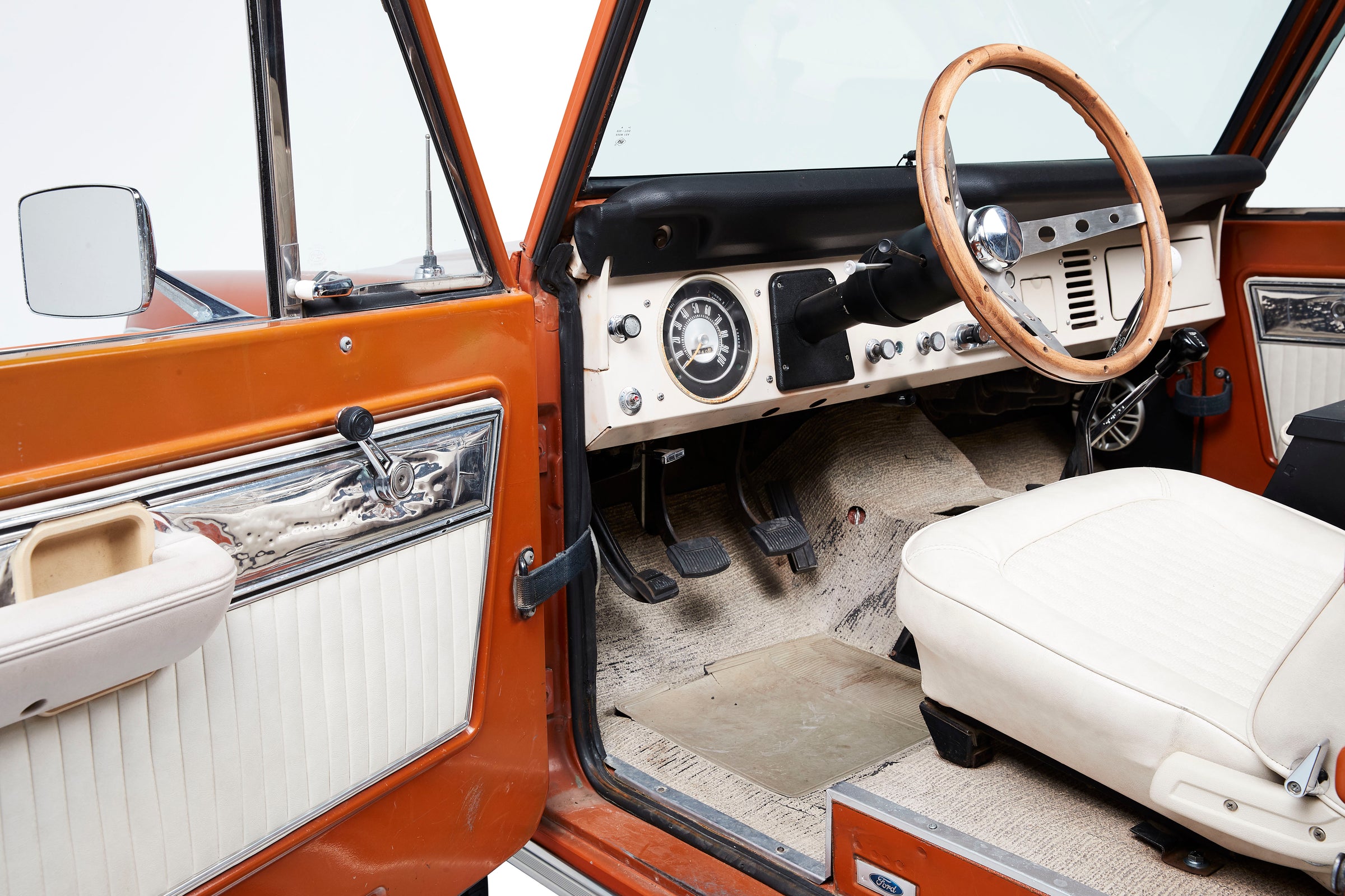Interior view of a classic Ford Bronco with a wooden steering wheel and orange door panel.