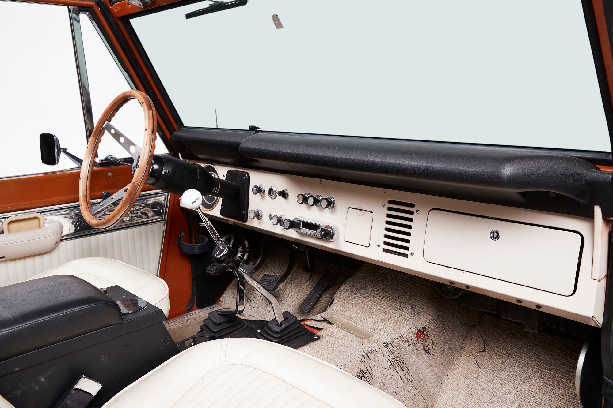 Interior dashboard and steering wheel of a Classic Ford Bronco with manual gear shifters and white seats.