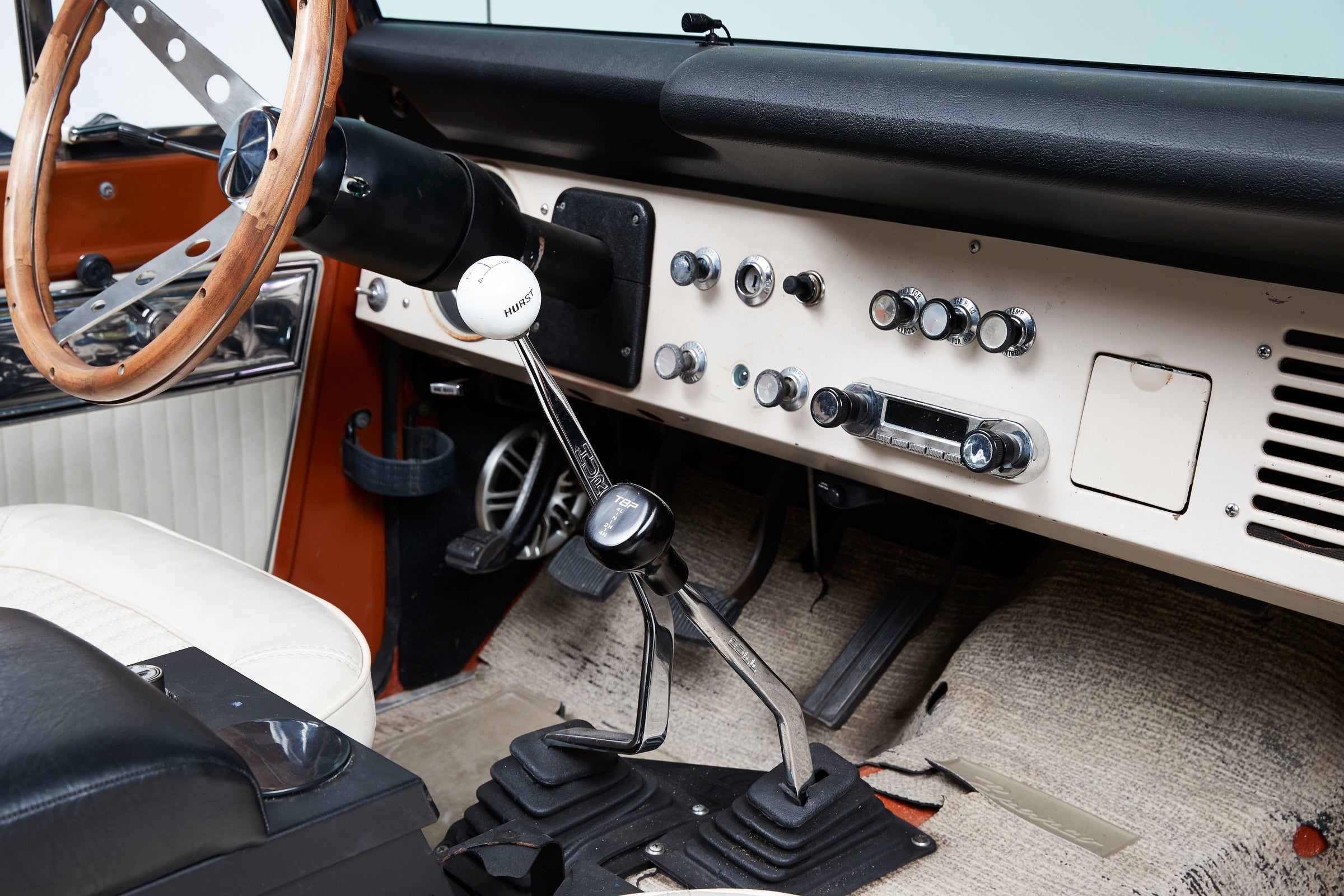 Interior view of a classic vehicle showing a wooden steering wheel, manual transmission shifters, and a beige dashboard with