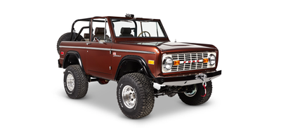 Brown Classic Ford Bronco side view showing off-road tires, chrome wheel rims, and open cabin with seats