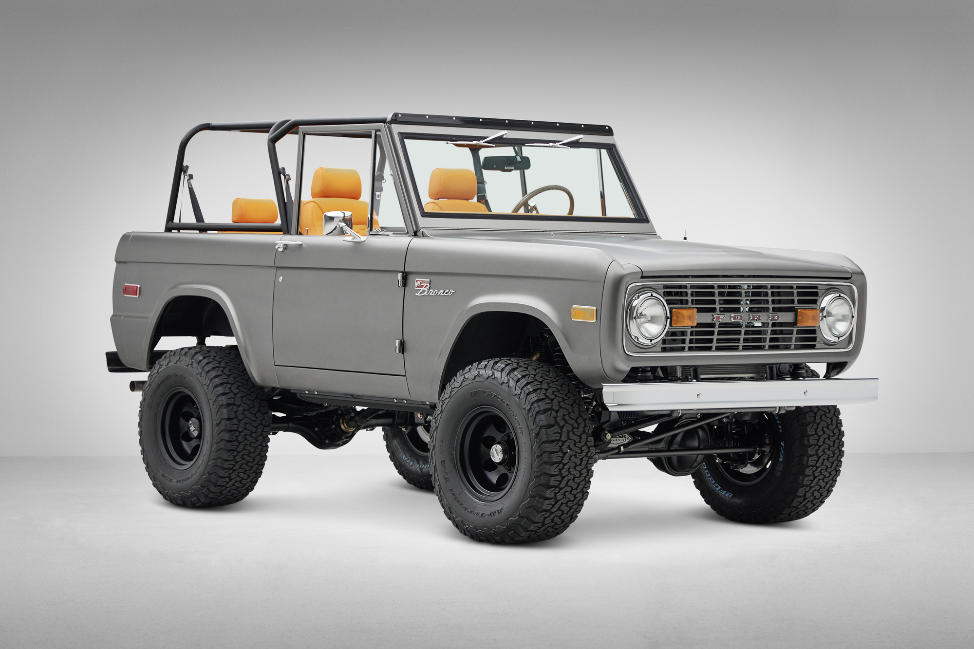 Classic Ford Bronco in matte silver with light interior and black wheels front passenger three-quarter view