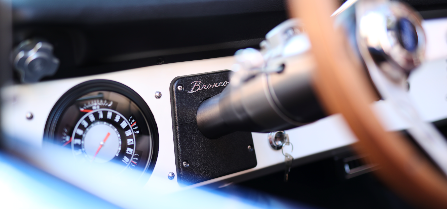 Close-up of Classic Ford Bronco dashboard with speedometer and Bronco emblem on white panel.