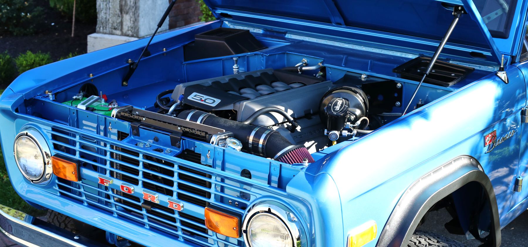 Classic Ford Bronco blue engine bay with 5.0 badge and open hood, showing detailed components.