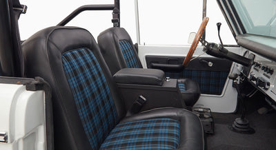 Interior view of Classic Ford Bronco showing black seats with blue plaid fabric inserts and wooden steering wheel