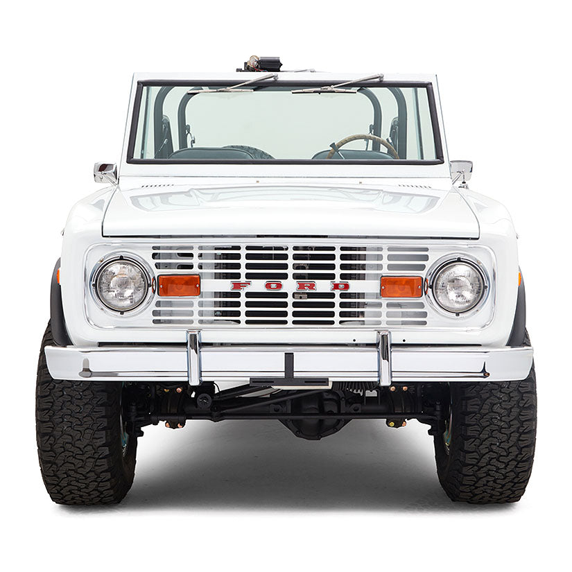 Front view of white Classic Ford Bronco with orange reflector lights and chrome bumper against white background