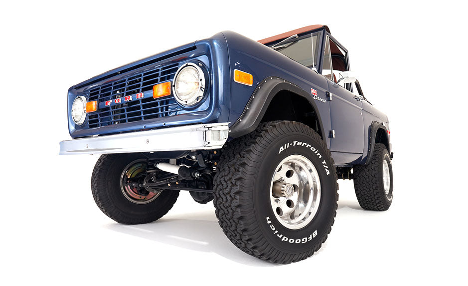 Low-angle front view of blue Classic Ford Bronco with raised suspension and all-terrain tires on white background