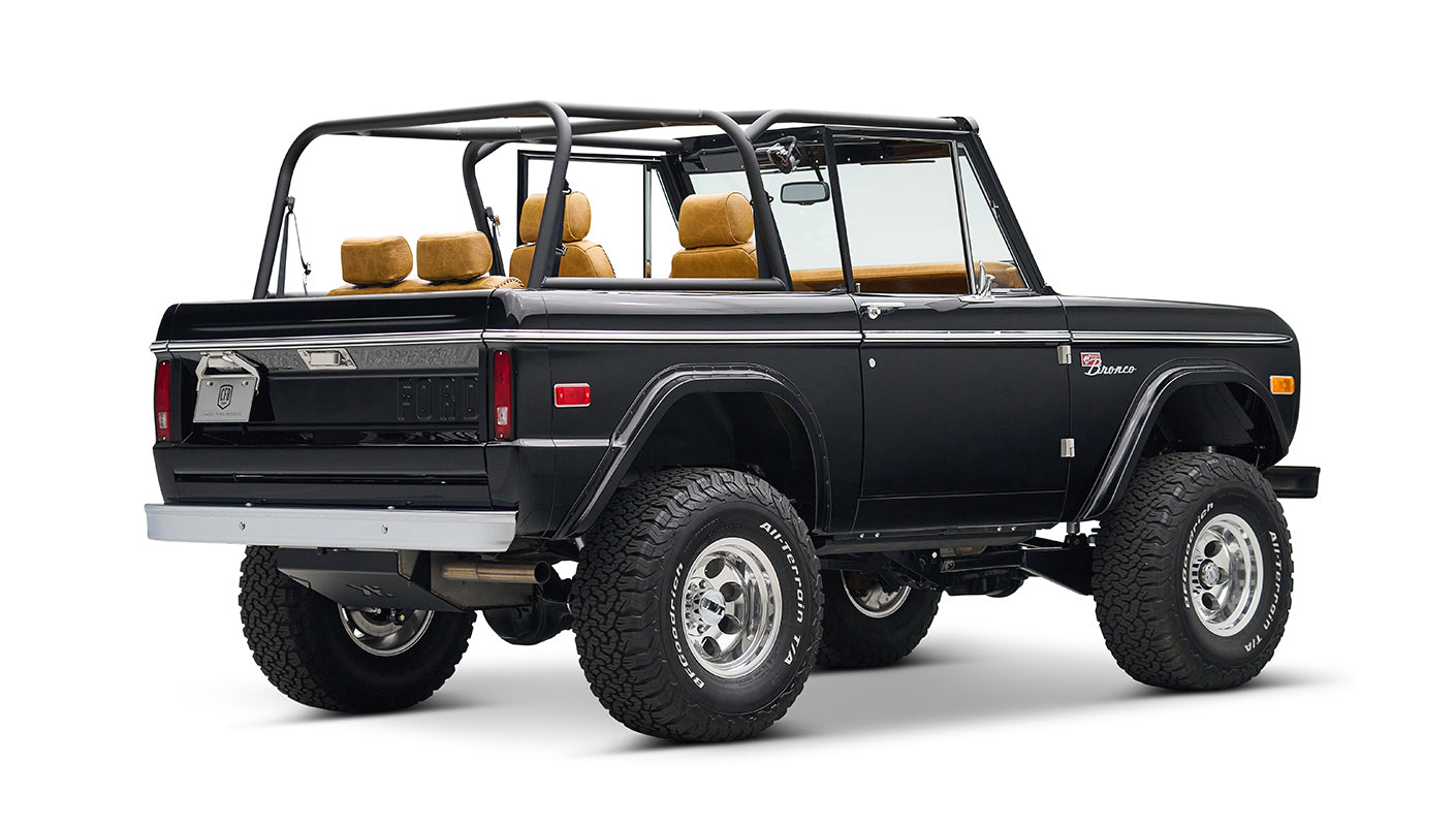 Rear quarter view of black Classic Ford Bronco with tan seats, chrome wheels, and lifted suspension