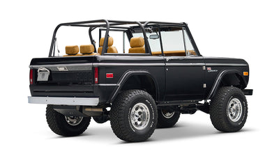 Rear quarter view of black Classic Ford Bronco with tan seats, chrome wheels, and lifted suspension