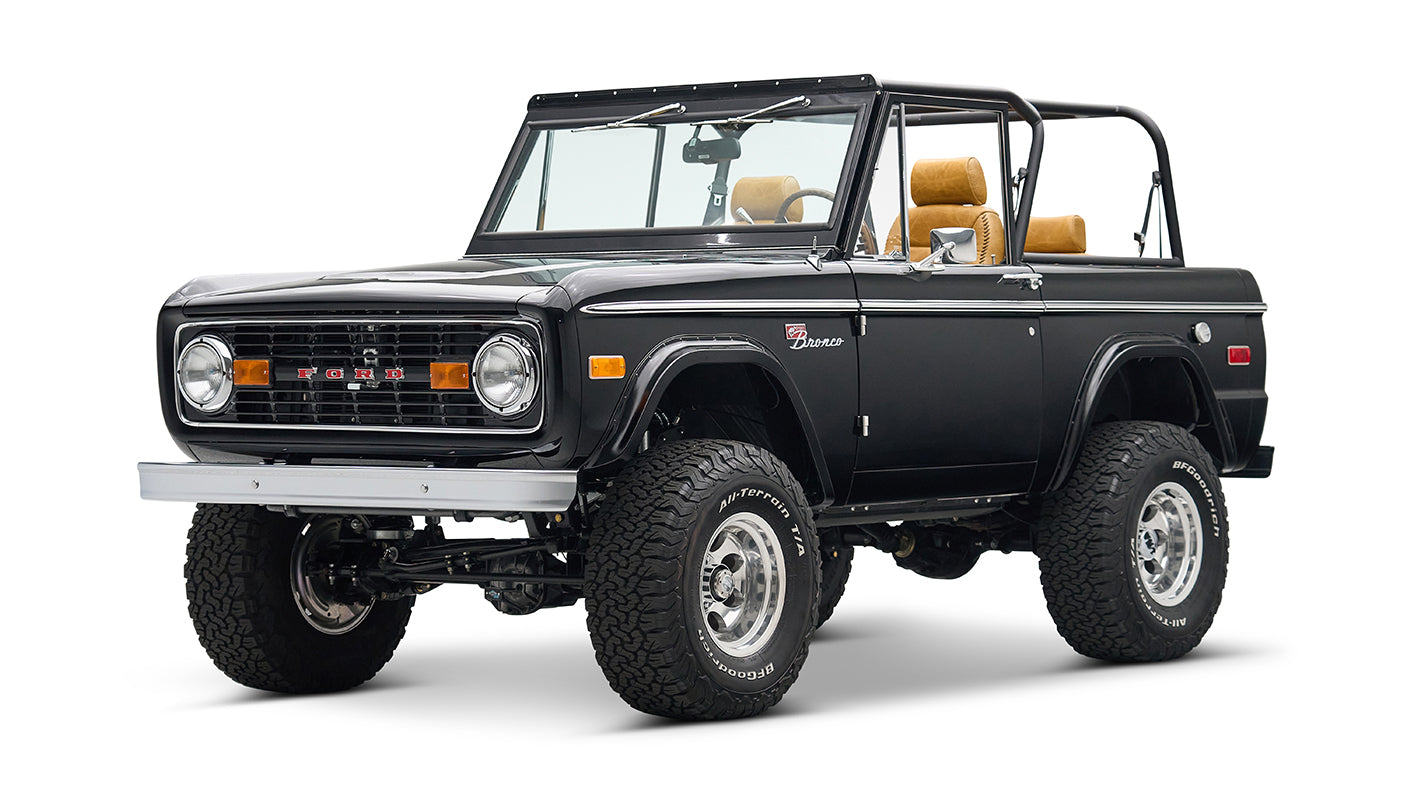 Black Classic Ford Bronco with tan seats, lifted suspension, and chrome wheels angled front right