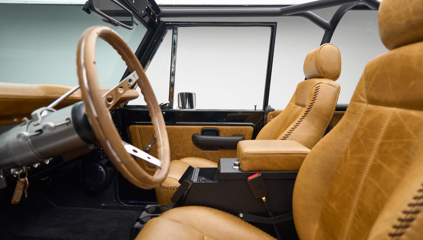 Interior of Classic Ford Bronco showing tan leather front seats, steering wheel, and door panel