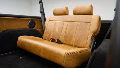 Rear tan leather bench seat of Classic Ford Bronco with seat belts and black roll bar