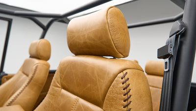 Two tan leather seat headrests with stitching details and black seat belt frame