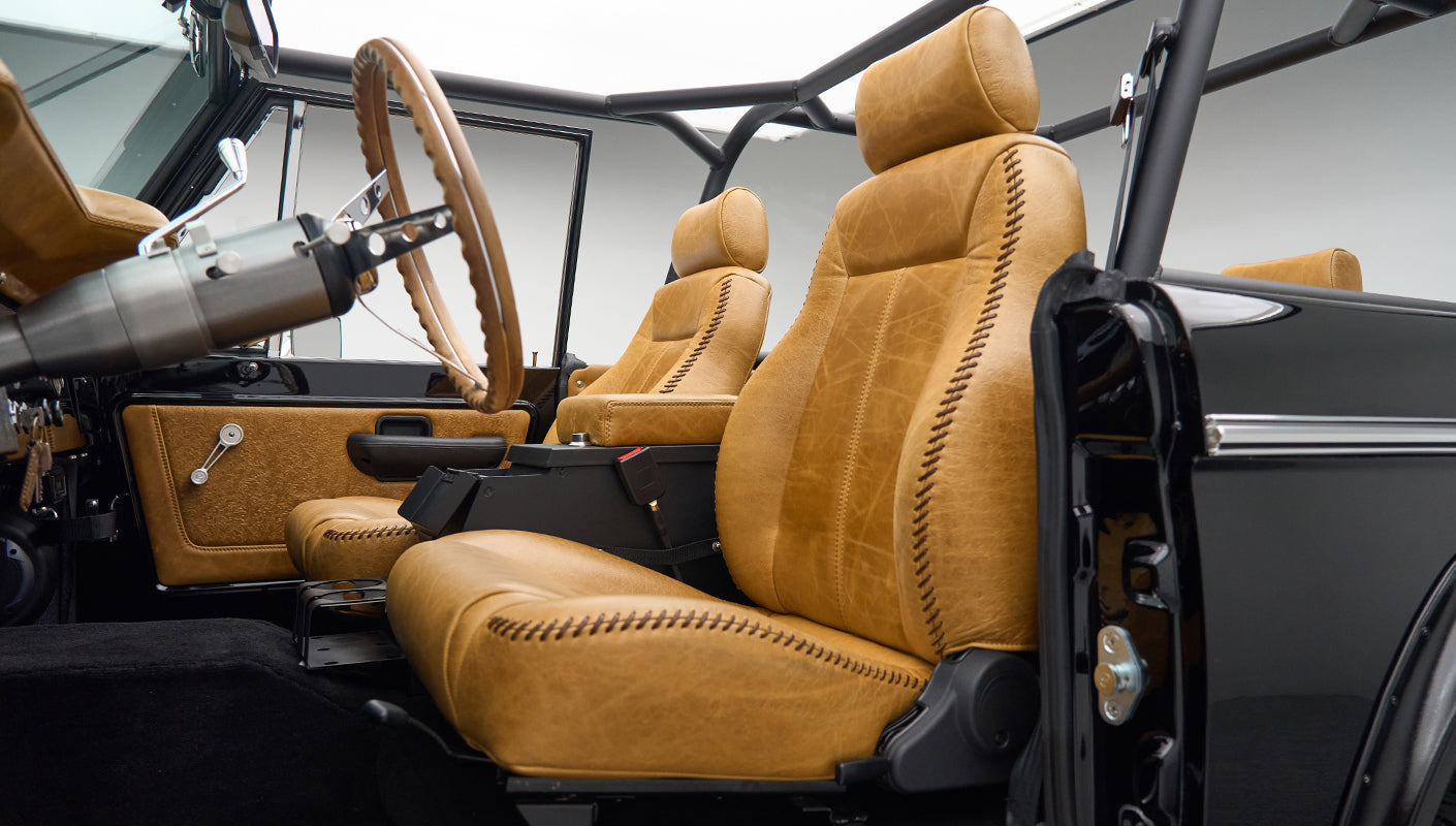 Side view of two tan leather seats with brown stitching inside a black vehicle interior