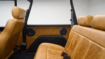 Side view of rear tan leather bench seat in Classic Ford Bronco with black roll bar and speakers