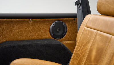 Interior side panel with tan embossed leather and black speaker next to black carpeted wheel well