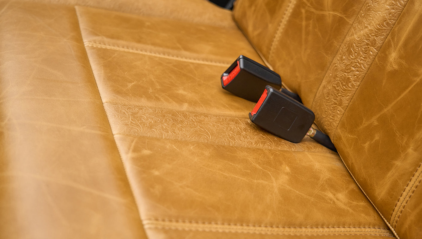 Close-up of tan leather seat cushion with two black seat belt buckles