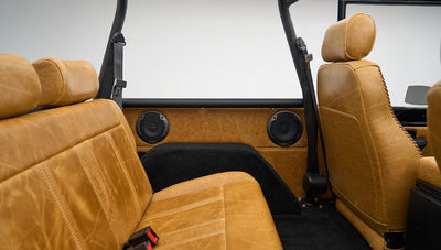 Classic Ford Bronco rear seat view showing tan leather upholstery, seat belts, and roll bar