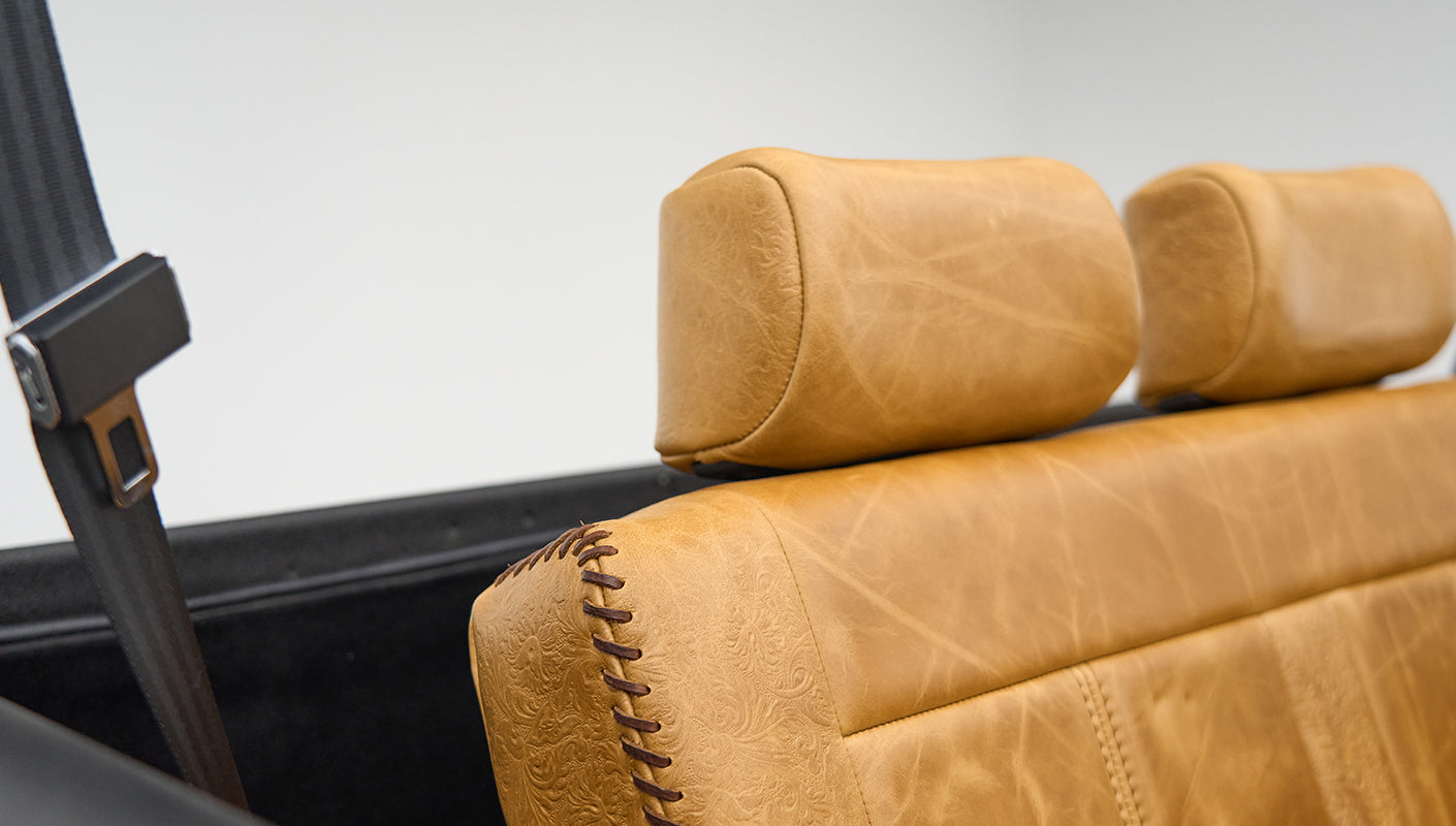 Tan leather seat headrest and side with decorative brown stitching and seat belt