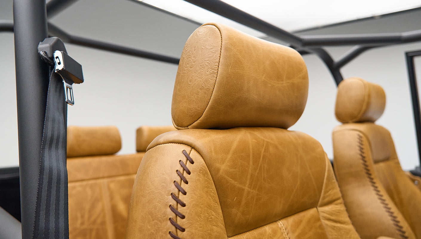 Tan leather upholstery and black safety belt inside Classic Ford Bronco with roll cage