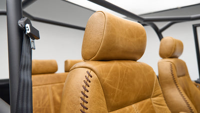Tan leather upholstery and black safety belt inside Classic Ford Bronco with roll cage