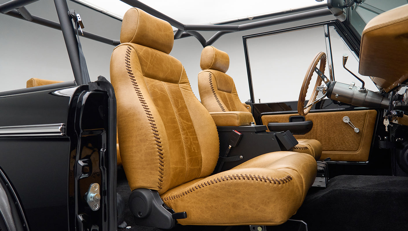 Side view of two tan leather seats and black seat belts inside a classic Ford Bronco interior