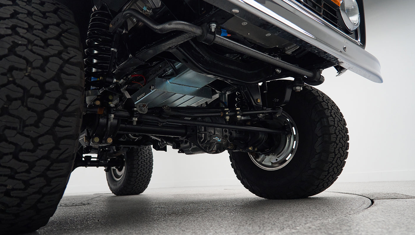 Underneath view of front axle, suspension, and large off-road tire on Classic Ford Bronco