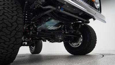 Underneath view of front axle, suspension, and large off-road tire on Classic Ford Bronco