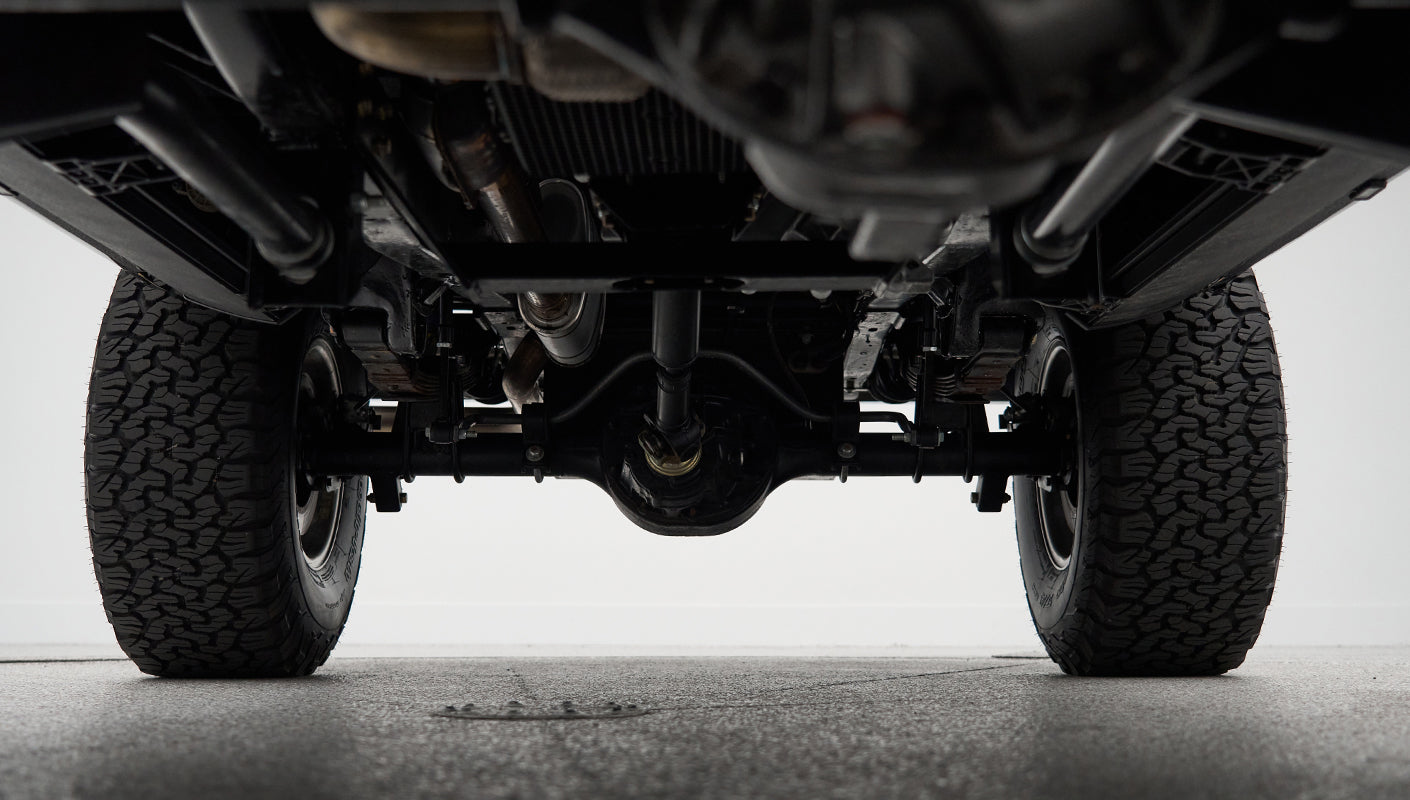 Underneath rear axle and suspension components with black off-road tires on Classic Ford Bronco