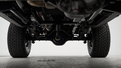Underneath rear axle and suspension components with black off-road tires on Classic Ford Bronco