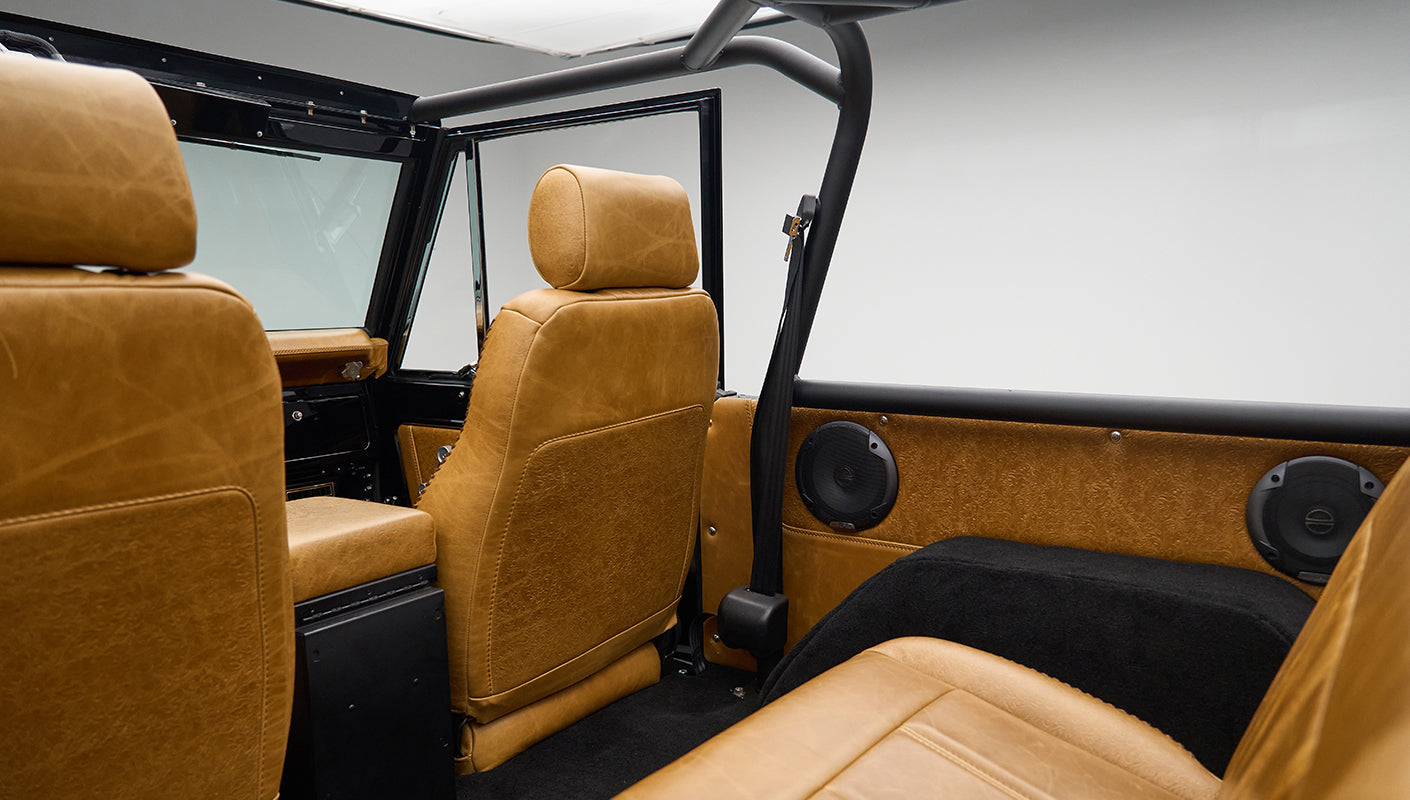 Rear interior view of Classic Ford Bronco showing tan leather seats and roll cage