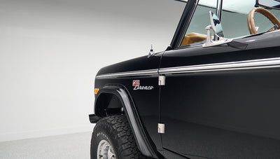 Front side view of black Classic Ford Bronco showing front wheel, fender, and door hinge