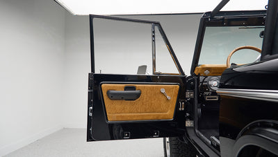 Open driver side door of black Classic Ford Bronco revealing tan leather door panel