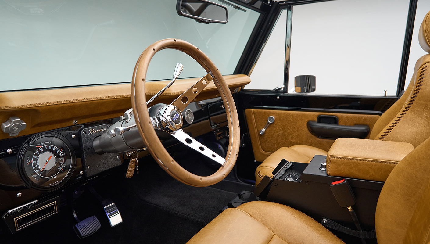 Classic Ford Bronco interior with tan leather seats and wood-trimmed steering wheel from driver side