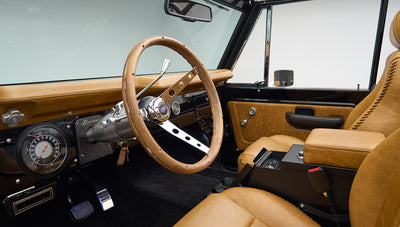 Classic Ford Bronco interior with tan leather seats and wood-trimmed steering wheel from driver side