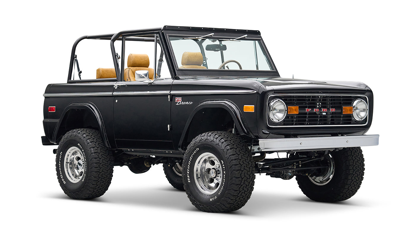 Black Classic Ford Bronco with tan seats, lifted suspension, and chrome wheels angled front left