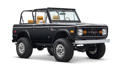 Black Classic Ford Bronco with tan seats, lifted suspension, and chrome wheels angled front left