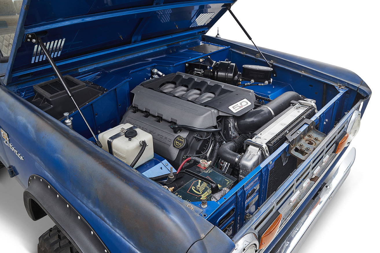 Open hood displaying a clean engine bay with a 5.0 badge engine inside a blue Classic Ford Bronco