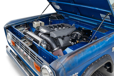 Open hood of blue Classic Ford Bronco showing 5.0 liter engine with clean components
