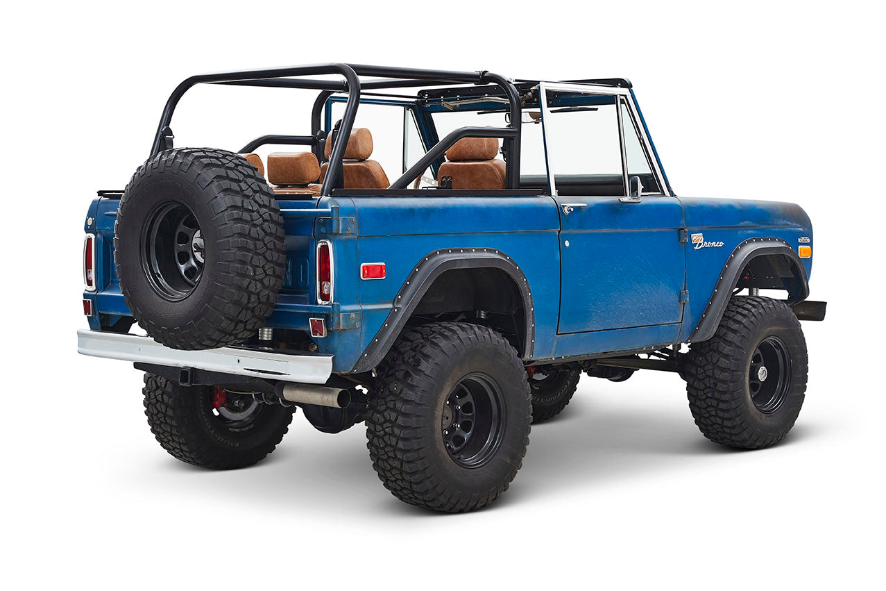 Three-quarter rear side view of a blue Classic Ford Bronco with exposed roll cage and large off-road tires