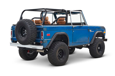 Three-quarter rear side view of a blue Classic Ford Bronco with exposed roll cage and large off-road tires