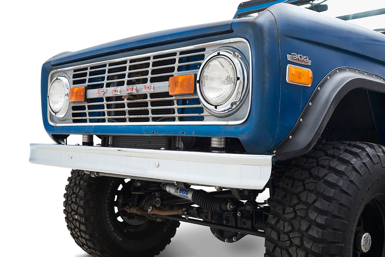 Close-up front corner of a blue Classic Ford Bronco showing headlight, orange turn signals, and tires
