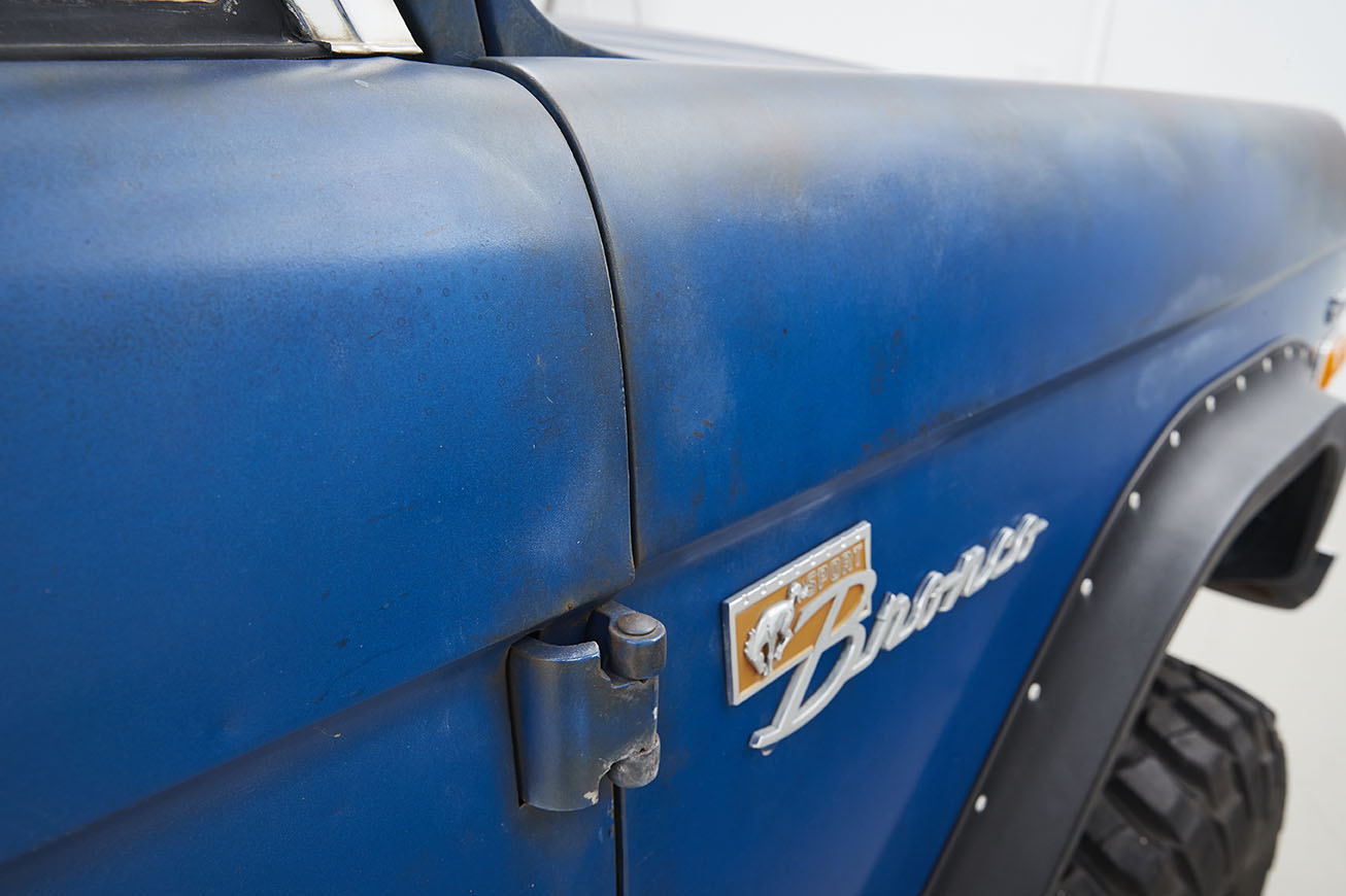 Close-up of blue Classic Ford Bronco side with rust and hood hinge visible